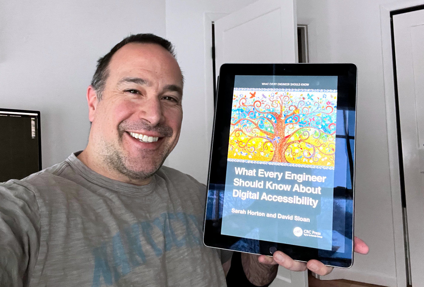 Ben Nadel holding an iPad that shows the cover of the book, What Every Engineer Should Know about Digital Accessibility, by authors Sarah Horton and David Sloan.