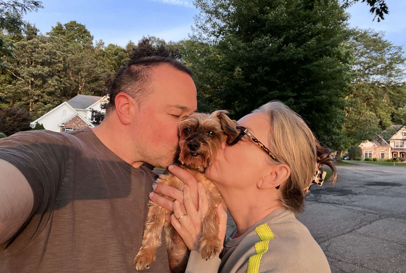 Ben and Mary Kate holding Lucy between their faces, kissing her cheeks, in a golden hour photo.